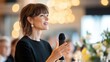 © Anna - Confident woman giving speech at elegant event with bright lighting and floral arrangements