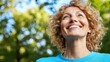 © imagineRbc - A woman with curly hair smiles brightly while standing outdoors in a park. Sunlight filters through the trees, creating a cheerful atmosphere in the afternoon