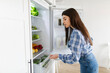 © Home-stock - Young woman searching food vegetables, opening refrigerator and planning what to cook for dinner. Meal preparation for dieting