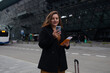 © Shi  - Business smiling 30s lady tourist woman with smart phone in casual clothing taking taxi from an airport. Luggage on the city street. Travel concept.