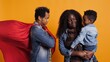 © DC Studio - African american dad being the superhero of his little toddler, posing as a hero with a red cape and saving his family from any danger. Cute loving family posing against yellow background. Camera B.