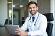 © Nina - Cheerful Male Doctor in White Coat with Stethoscope at Modern Office Desk Working on Laptop, Smiling Professional in Healthcare Setting
