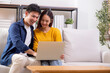 © NT_studio - Young asian couple looking on laptop for relax with cozy and contentment sitting on sofa in living room at home, couple leisure watching laptop on couch, relationship and bonding, lifestyle concept.