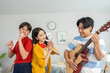 © Pavitra - Diverse Asian friends playing guitar and dancing in living room at home.