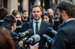 © saichon - A well-dressed man speaks to reporters surrounded by cameras and microphones, capturing a moment of media attention in a bustling urban setting.