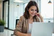 © MT - A young Hispanic woman in a modern office setting, smiling while working on her laptop, surrounded by natural light and greenery, emphasizing a professional and inviting atmosphere.