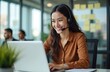 © miss irine - Young woman in headset working on laptop in office. Smiling hispanic businesswoman types on computer keyboard during video call. Help desk employee assists client. Online support service at workplace.