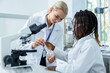 © zinkevych - Blonde woman in lab coat explaining to a student how to sue microscope