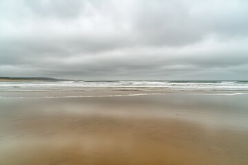 Poster - Lonely seashore with gentle waves and an overcast sky inviting calm reflections in open space Generative AI