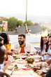 © Xavier Lorenzo - Vertical shot of happy diverse group of friends enjoying dinner barbecue and drinking wine in summer at home terrace