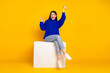 © deagreez - Young woman in casual attire joyfully posing on a block against bright yellow background