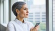 © Thuntaree - Woman with Short Gray Hair Holding Smartphone by Window