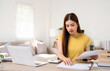 © Fahng - Young asian female work with financial papers at home count on calculator before paying taxes receipts online by laptop. woman planning budget glad to find chance for economy saving money.