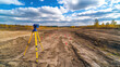 © Саша Федюк - A surveying instrument is positioned on a yellow tripod in a cleared area. Bright orange markers are placed along the dirt pathway
