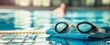 © BerkahStock - Swimming goggles and towel by the poolside. (1)