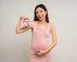 © Chanakon - Happy Pregnant asian woman stroking touch belly motherhood with tiny kids pink shoes on isolated background. Family planning maternity and pregnancy with insurance for child health.