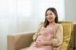 © Chanakon - Happy pregnant woman caresses her belly while taking rest on sofa at home, concept of happy motherhood waiting for childbirth, family planning and pregnancy with insurance for child health.
