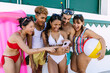 © Xavier Lorenzo - Group of cheerful diverse friends looking excitedly at smartphone while enjoying summer vacation together at a beach house. Social media and vacation concept