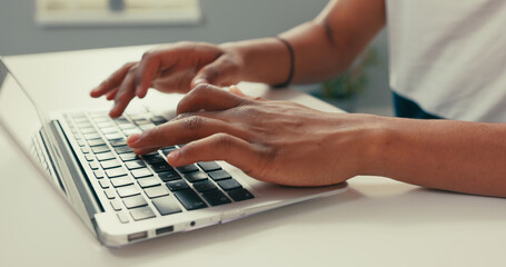Close-up of silver latop standing on white desk, dark-skinned man working on it, young hands, typing text into keyboard, tapping fingers on computer