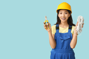 Wall Mural - young female electrician with pliers and cables on blue background