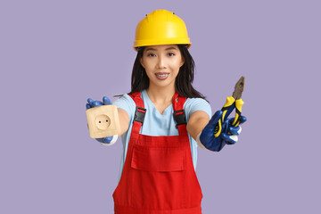 Wall Mural - young female electrician with pliers and socket on purple background