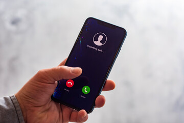Close-up of a hand holding a smartphone with an incoming call screen. Display shows Incoming call with green accept and red decline buttons.