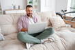 © Pixel-Shot - Freelance worker sitting on sofa and using laptop at home