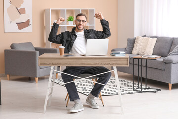 Young man sitting at workplace with raised hands at home