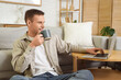 © Pixel-Shot - Young man drinking coffee and using laptop at home