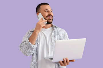 Wall Mural - young man with laptop talking on mobile phone on lilac background