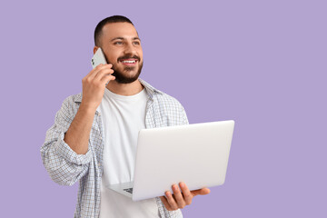 Wall Mural - young man with laptop talking on mobile phone on lilac background