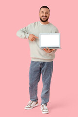 Wall Mural - young man pointing at laptop on pink background