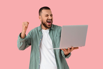 Wall Mural - cheering young man with laptop on pink background