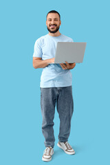 Wall Mural - smiling young man with laptop on blue background