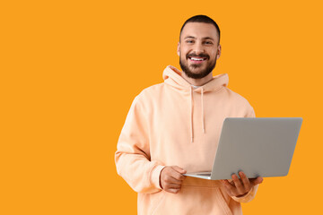 Wall Mural - smiling young man with laptop on yellow background