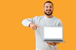 © Pixel-Shot - Young man pointing at laptop on yellow background