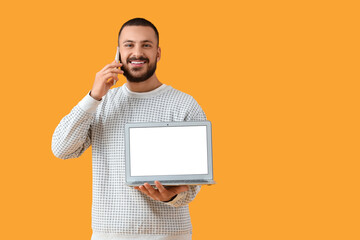 Wall Mural - young man with laptop taking on mobile phone on yellow background