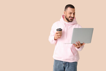 Wall Mural - young man with laptop drinking coffee on beige background