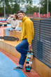 © zinkevych - Tall guy in yellow hoodie standing with skateboard in hands