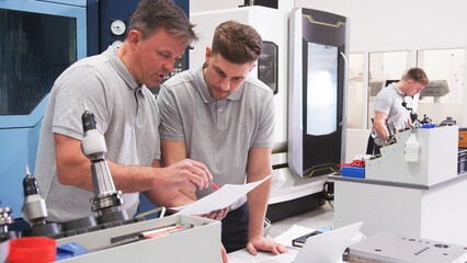 Wall Mural - male engineer and apprentice discussing plans for job whilst looking at laptop
