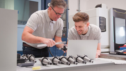 Wall Mural - male engineer and apprentice measuring components whilst looking at laptop
