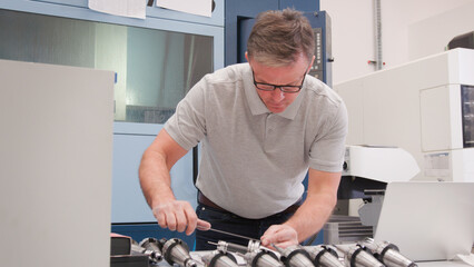 Wall Mural - mature male engineer in factory using cad programming software on laptop measuring component
