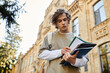 © LIGHTFIELD STUDIOS - Stylish young man outside an old university building taking notes and studying materials