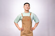 © Daniel - A cheerful Asian barista wearing a brown apron over a mint green shirt smiles warmly while placing his hands on his stomach against a white background, conveying friendliness, hospitality