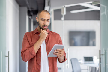 serious thinking programmer developer standing with tablet computer in hands. man testing new applic