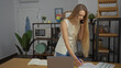 © Krakenimages.com - Woman talking on phone while writing in modern office setting with laptop and documents on desk and minimal decor in background showcasing professional environment.