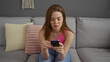 © Krakenimages.com - Woman sitting on a couch at home using a smartphone in a modern living room