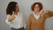 © Krakenimages.com - Women expressing different opinions with thumbs up and down against a white wall, showcasing diverse reactions among two middle-aged friends on an isolated background.