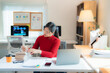 © Tj - Young Asian businesswoman wearing red turtleneck sweater sitting at desk and checking financial report, working with documents and laptop in modern office, business and finance concept