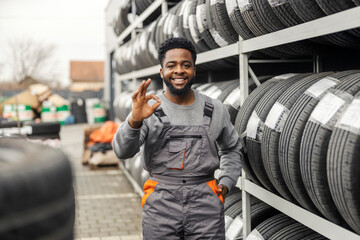 Fototapete - Portrait of interracial auto mechanic worker standing near tires and gesturing okay at camera.